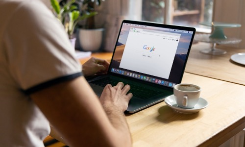 Uomo che a colazione cerca su Google su un laptop nero con un caffè a fianco